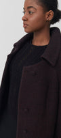 A woman wearing a burgundy baby alpaca coat over a black knit sweater.