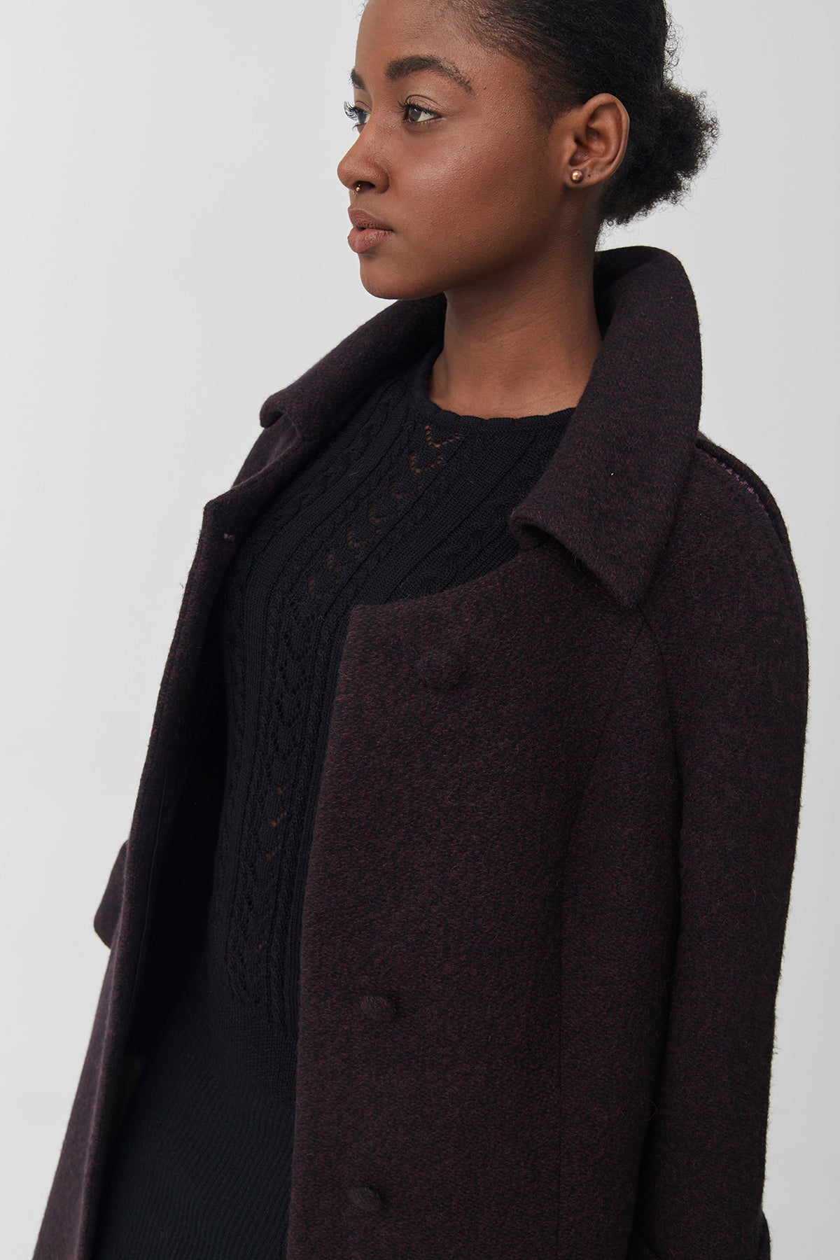 A woman wearing a burgundy baby alpaca coat over a black knit sweater.