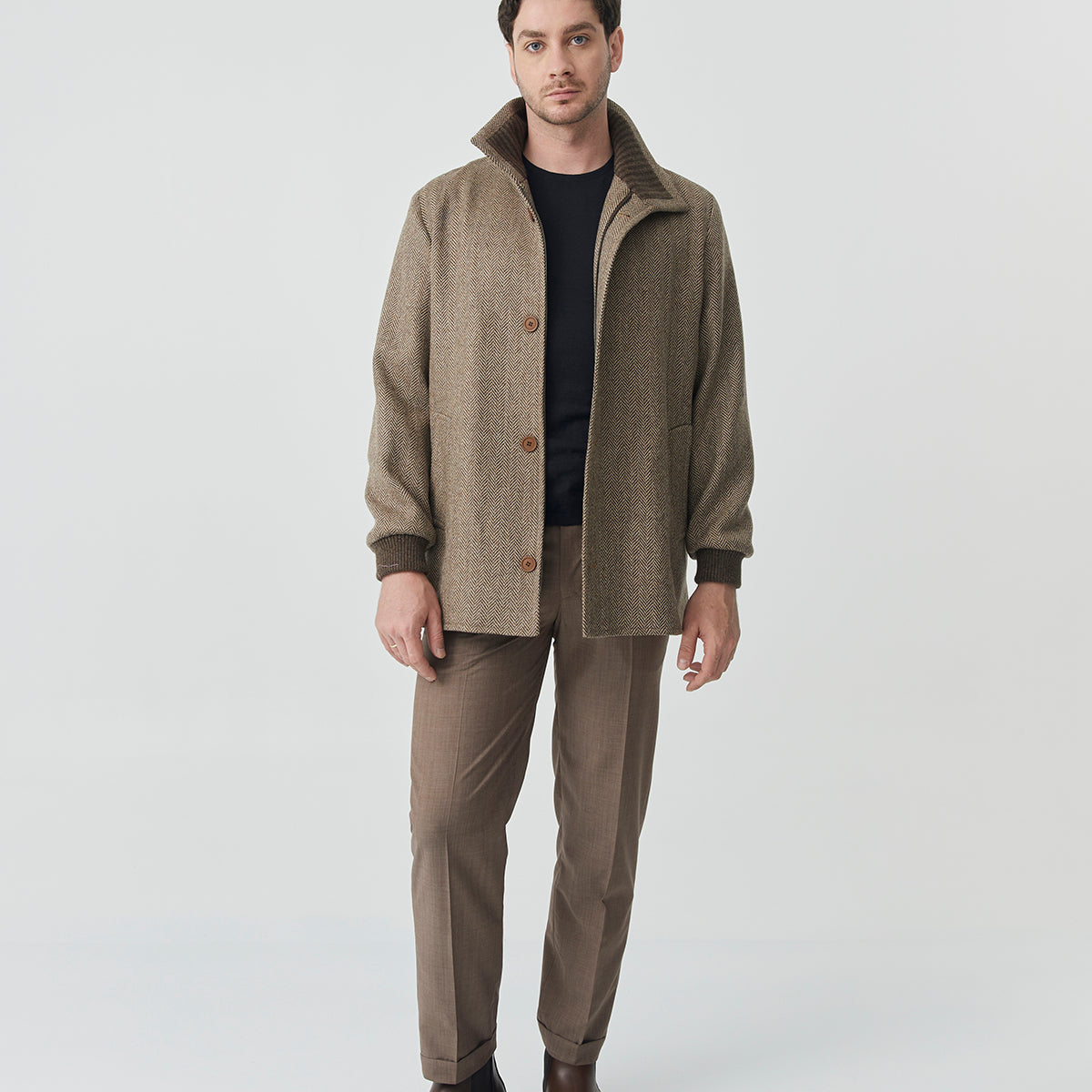 Man wearing a brown herringbone tweed jacket with front buttons and a high collar.