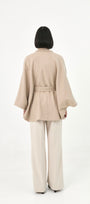 A model viewed from behind wearing a beige baby alpaca cape with a high ribbed collar and a matching belt.