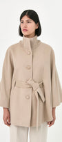 A model wearing a beige baby alpaca cape with a matching belt, buttons front, and side pockets.