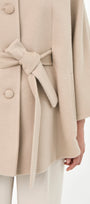 Close-up of a beige baby alpaca cape with a matching belt, buttons front, and side pockets.