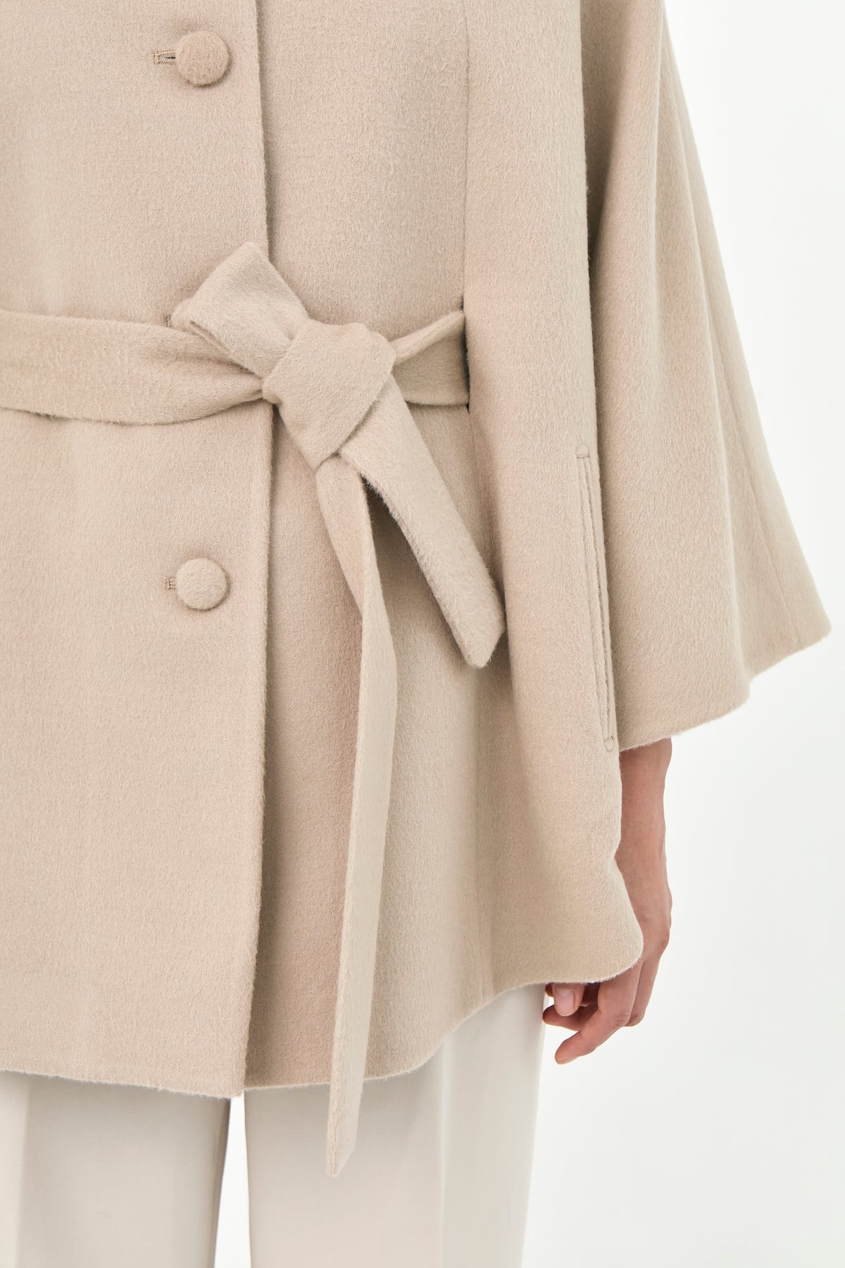 Close-up of a beige baby alpaca cape with a matching belt, buttons front, and side pockets.