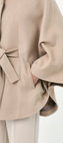 A close-up of a beige baby alpaca cape with a wiast tier, buttons front, and side pockets.