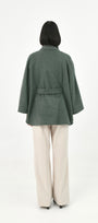 A model shown from the back wearing a green baby alpaca cape with a matching waist tie.