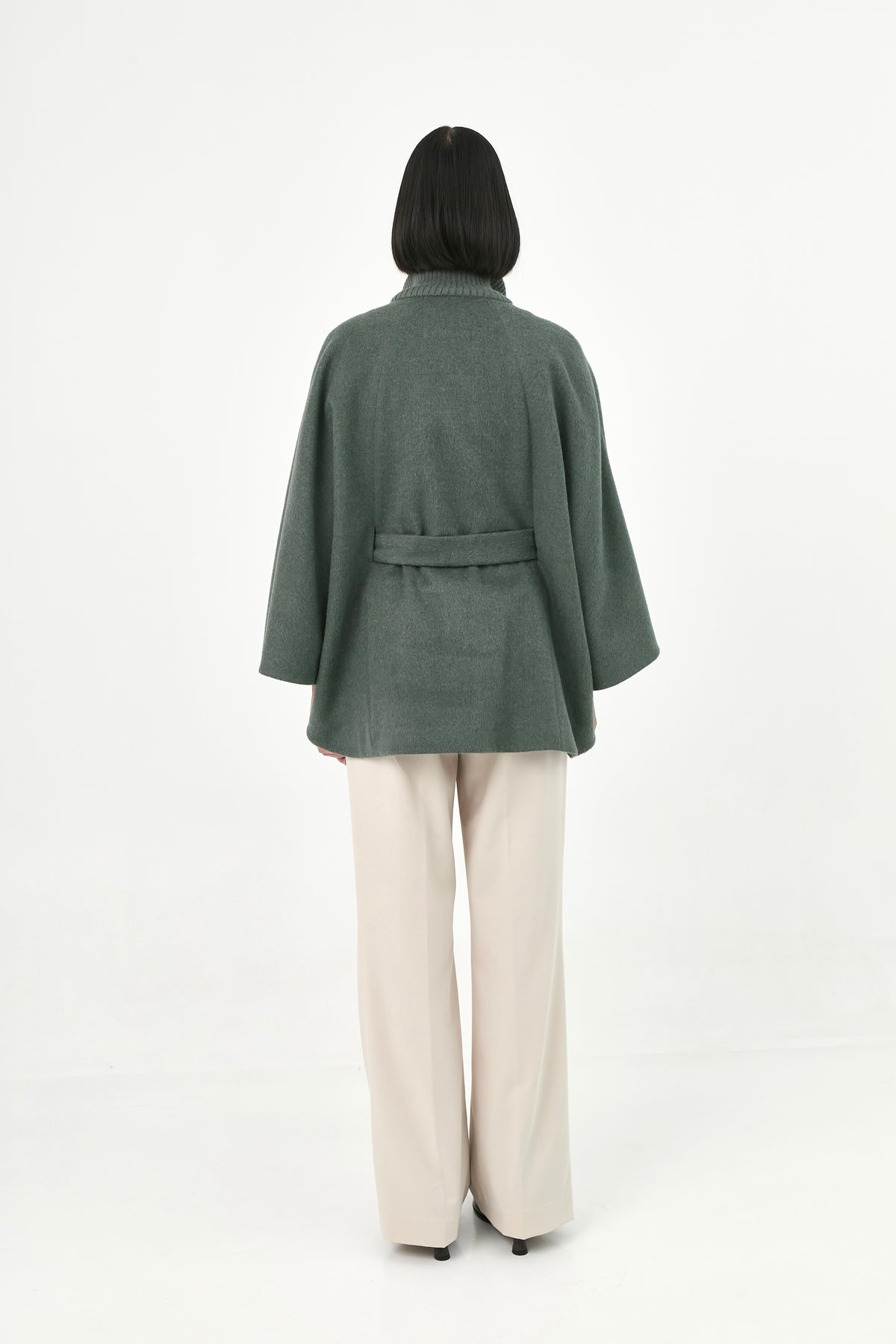 A model shown from the back wearing a green baby alpaca cape with a matching waist tie.
