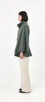 A model shown from the side profile wearing a green baby alpaca cape with a high ribbed stand collar.