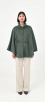 A model wearing a green baby alpaca cape with a high ribbed stand collar, buttons front, and matching waist tie.