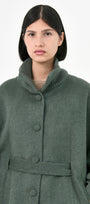 A model wearing a green baby alpaca cape with a high ribbed stand collar, buttons front, and matching waist tie.