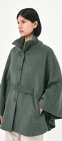 A model wearing a green baby alpaca cape with a high ribbed stand collar, buttons front, and matching waist tie.