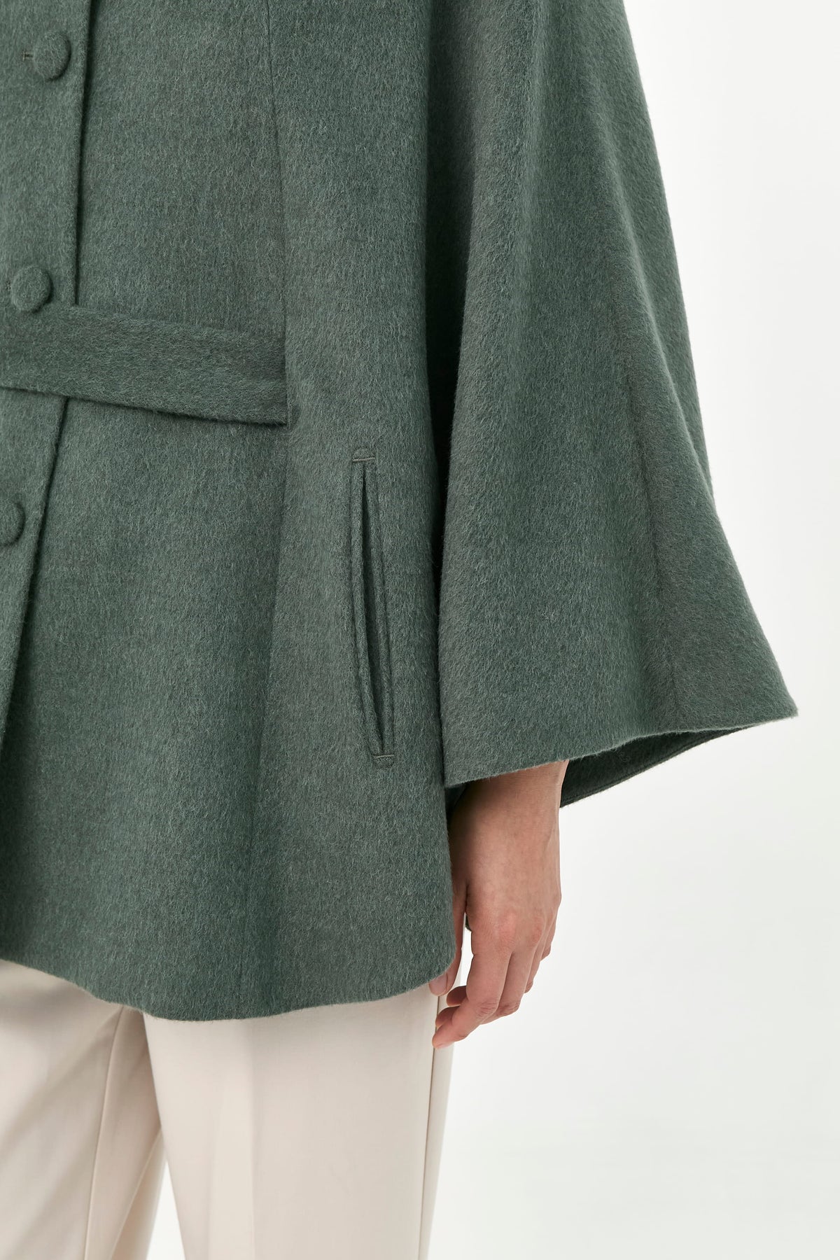 Close-up of a green baby alpaca cape with side pockets and a belt.