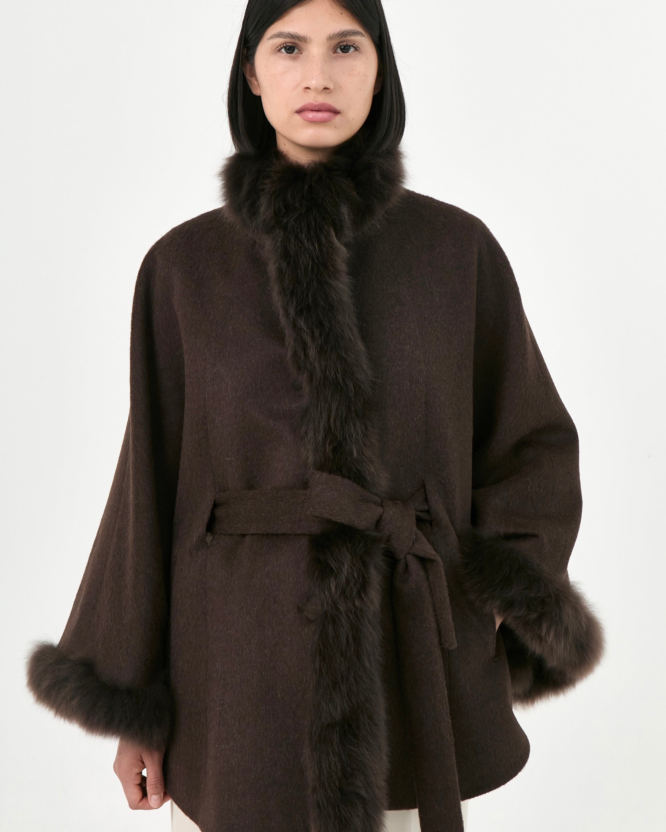 A model wearing a dark brown baby alpaca cape with a matching fur collar and cuffs, paired with a belt.
