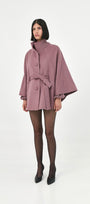 A model wearing a mauve baby alpaca cape with a high ribbed collar and a belted waist.