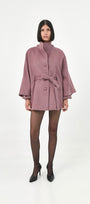 A model wearing a mauve baby alpaca cape with a high ribbed turtleneck collar and a belted waist.