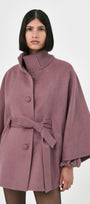 A model wearing a rose mauve baby alpaca cape with a turtleneck ribbed collar and a belt.