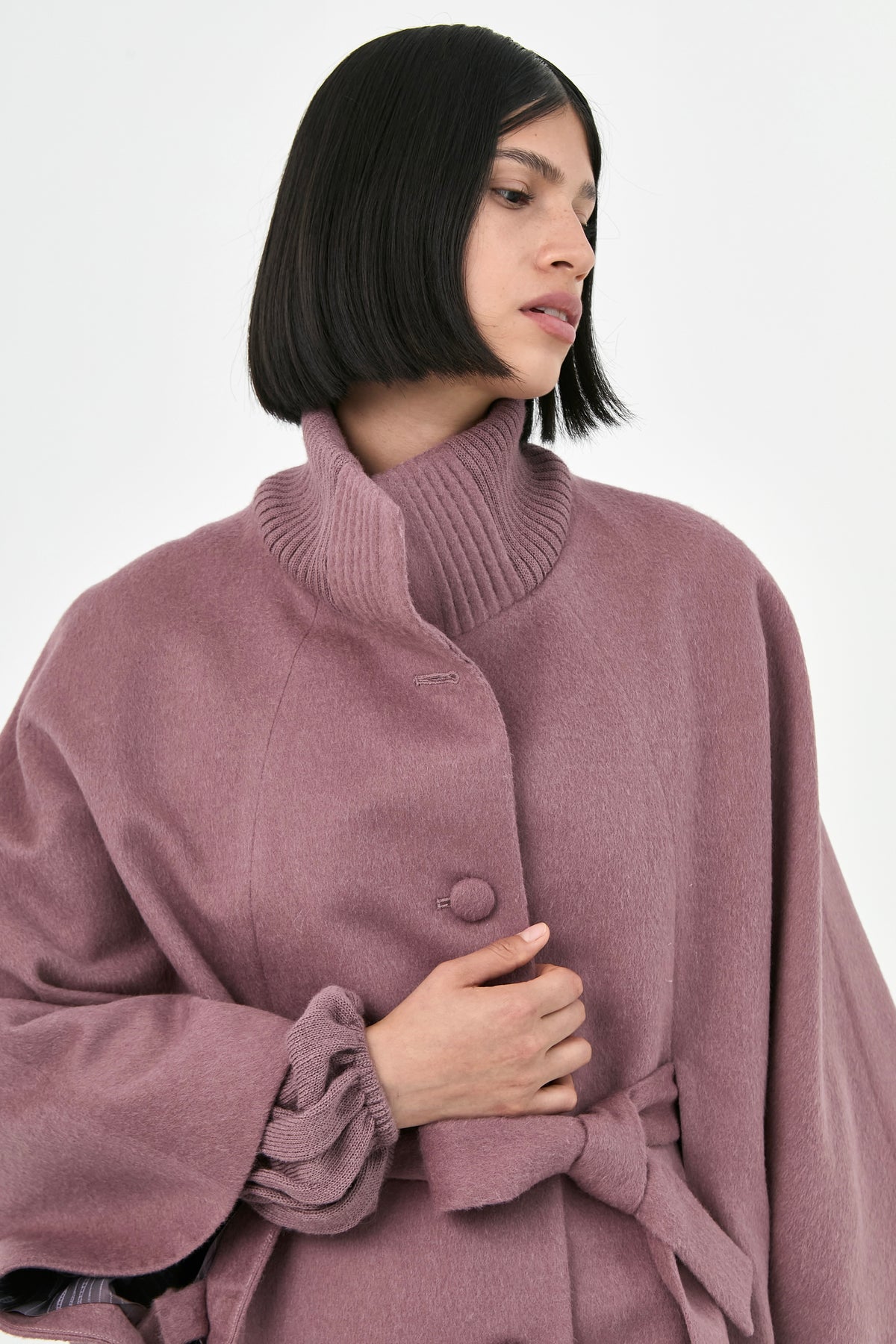 A model wearing a rose mauve baby alpaca belted cape with a ribbed turtleneck collar.