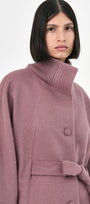 A model wearing a mauve baby alpaca cape with a high ribbed turtleneck collar, and a belted waist.