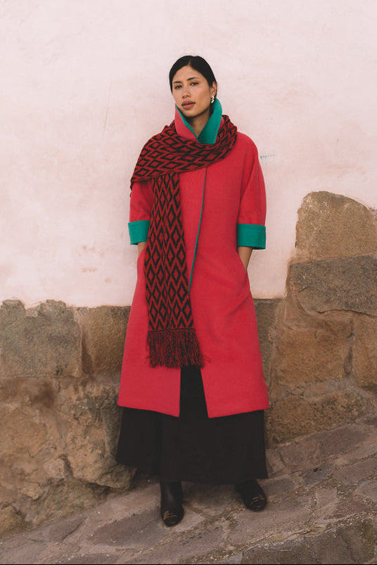 Woman wearing a fuchsia coat and patterned scarf against a stone wall.